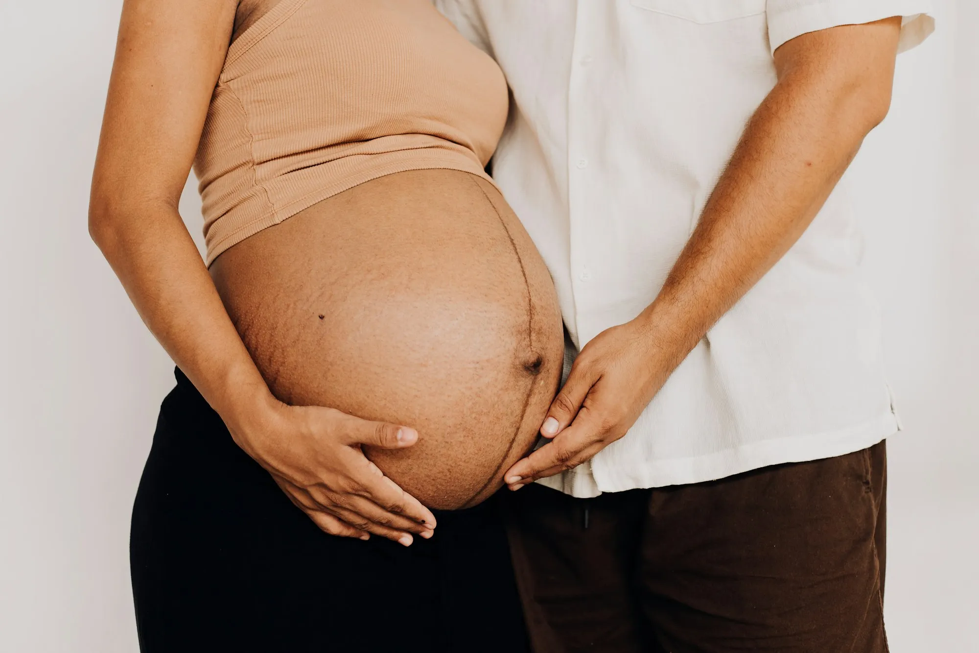 Man and pregnant woman standing side by side, both with a hand on her bump