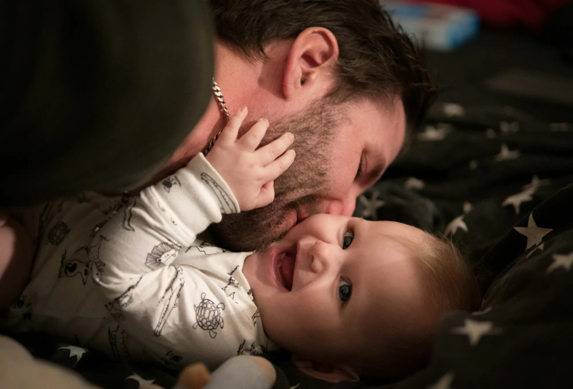 Dad lying in bed nose to nose with his laughing baby