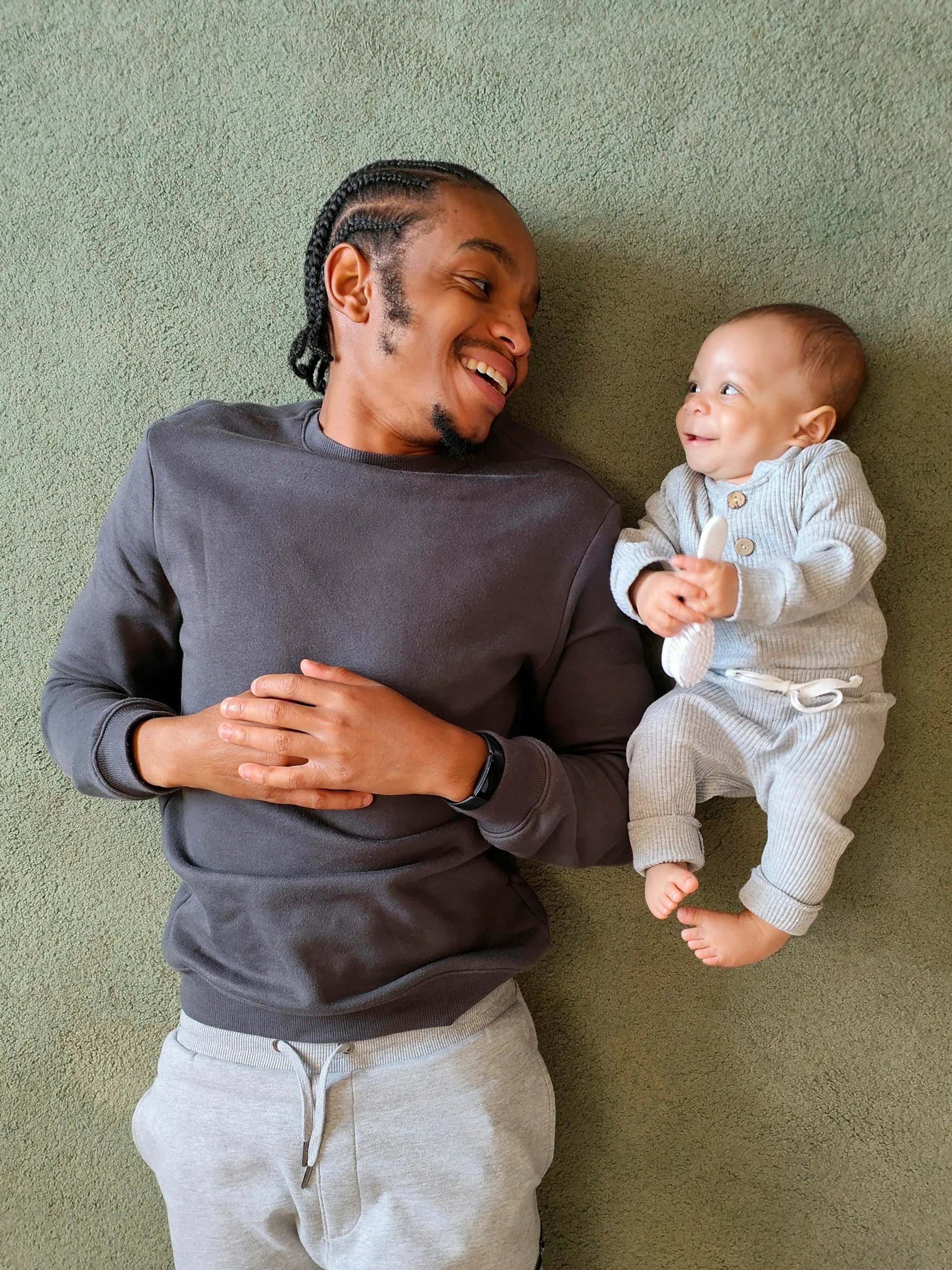 Smiling dad lying on the carpet next to his baby