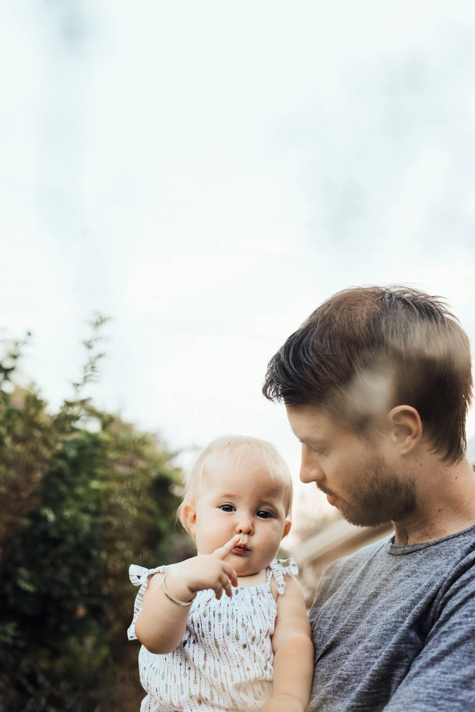 Dad holding his baby outside, both looking at something off camera