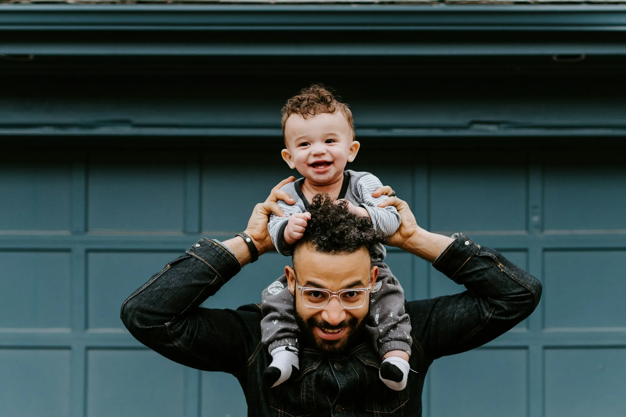 Laughing dad with his baby sitting on his shoulders in front of a blue door