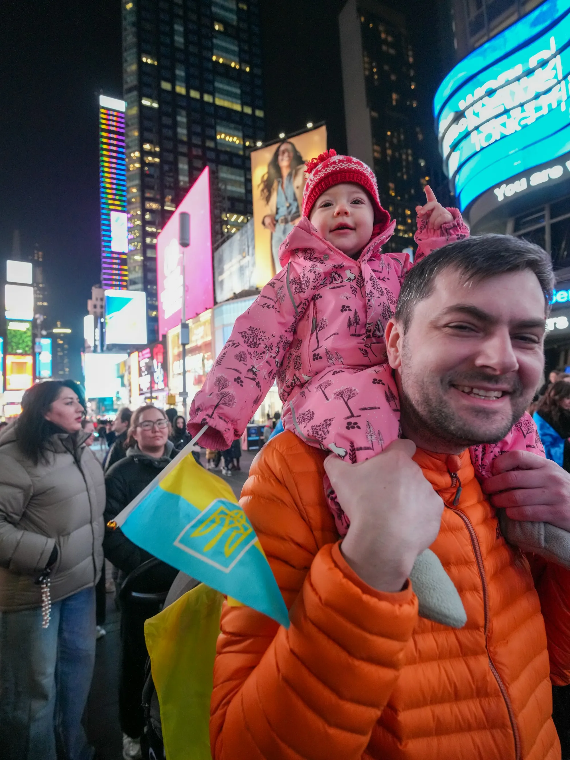 Smiling dad carrying his baby on his shoulders in Times Square at night
