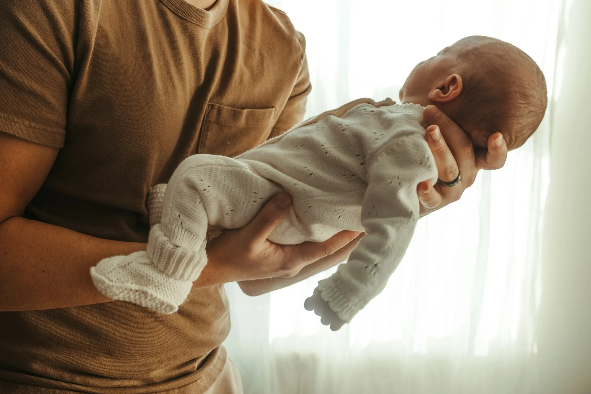 Dad holding a newborn in his arms in front of a bright window