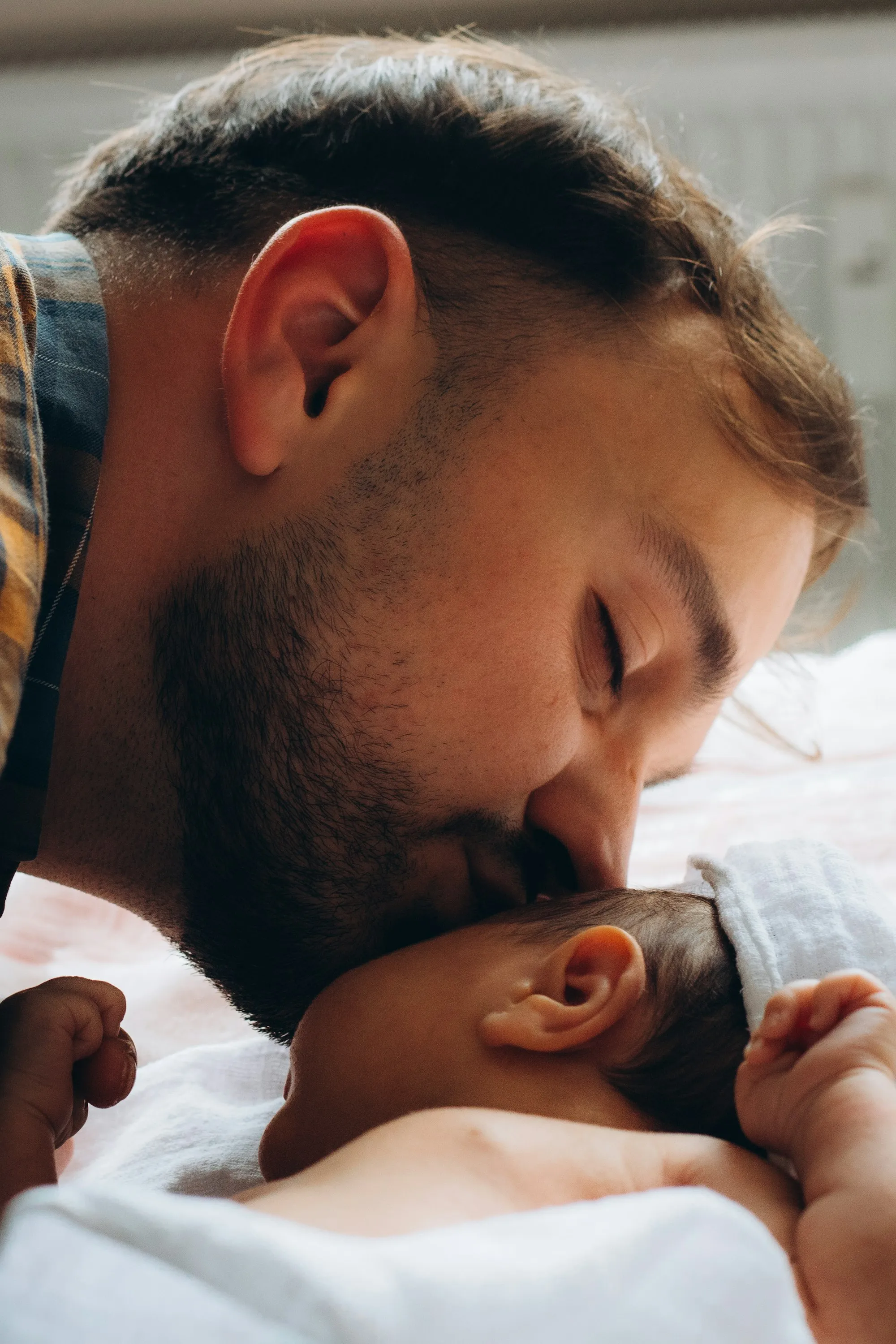 Bearded dad kissing his sleeping newborn on the forehead