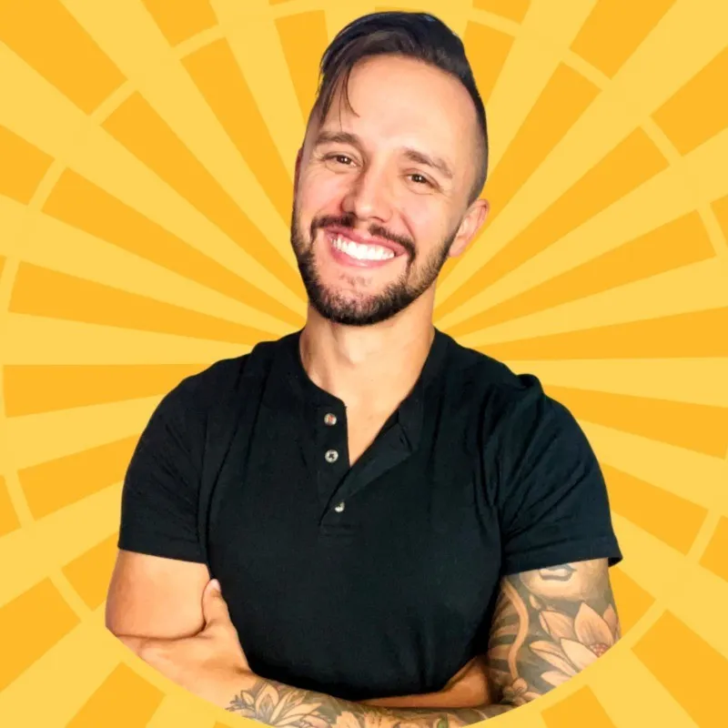 Smiling bearded man with tattooed arms crossed in front of a yellow sunburst background