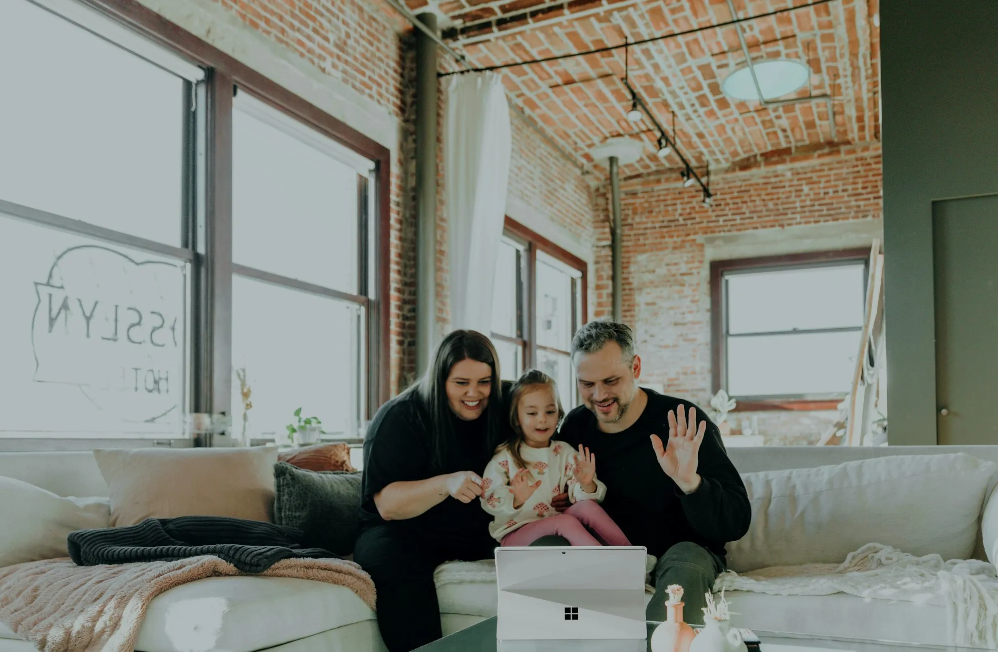 Mom, dad and their toddler on a sofa, smiling at a laptop on the coffee table