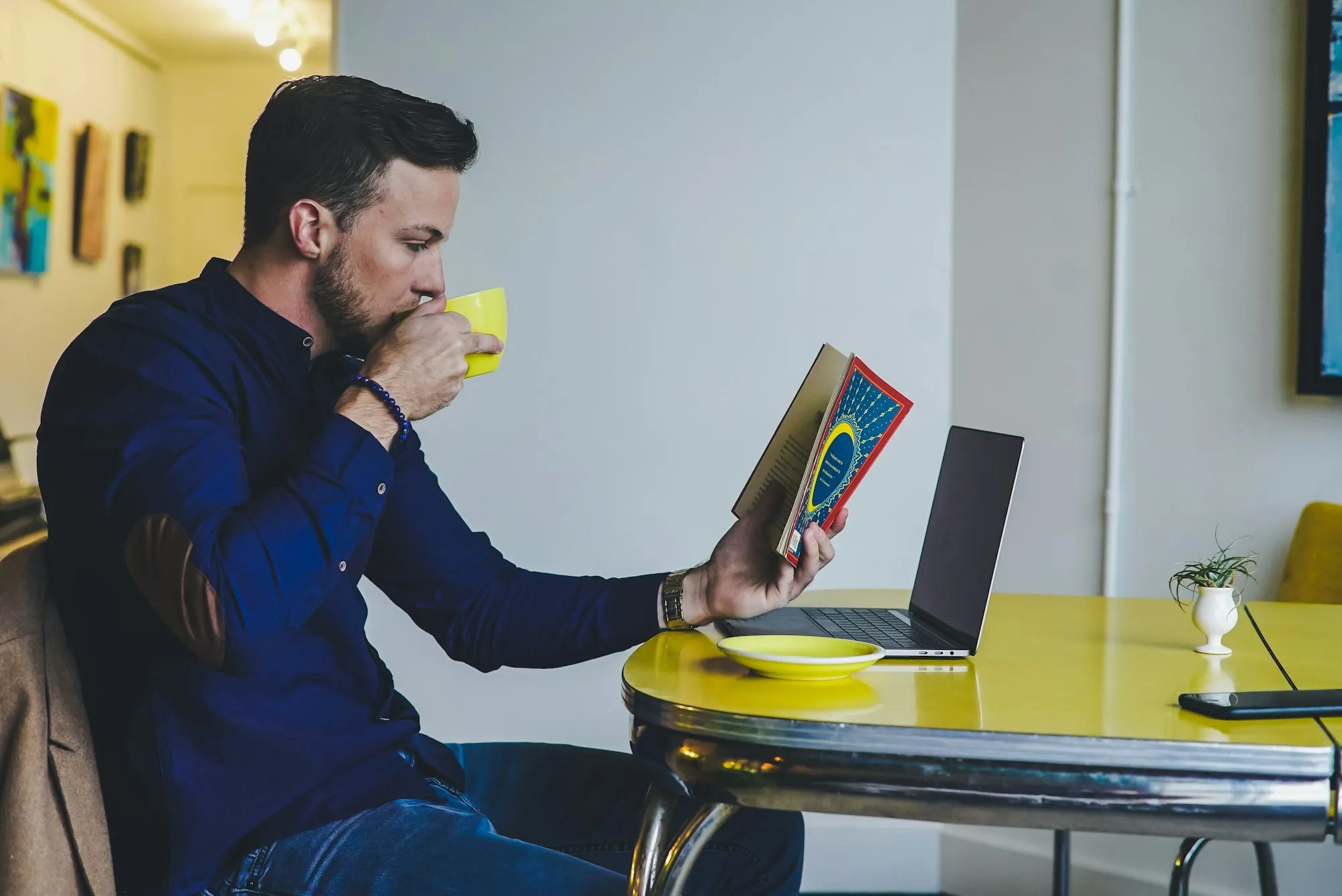 Bearded man reading a book with a cup of coffee at a kitchen table
