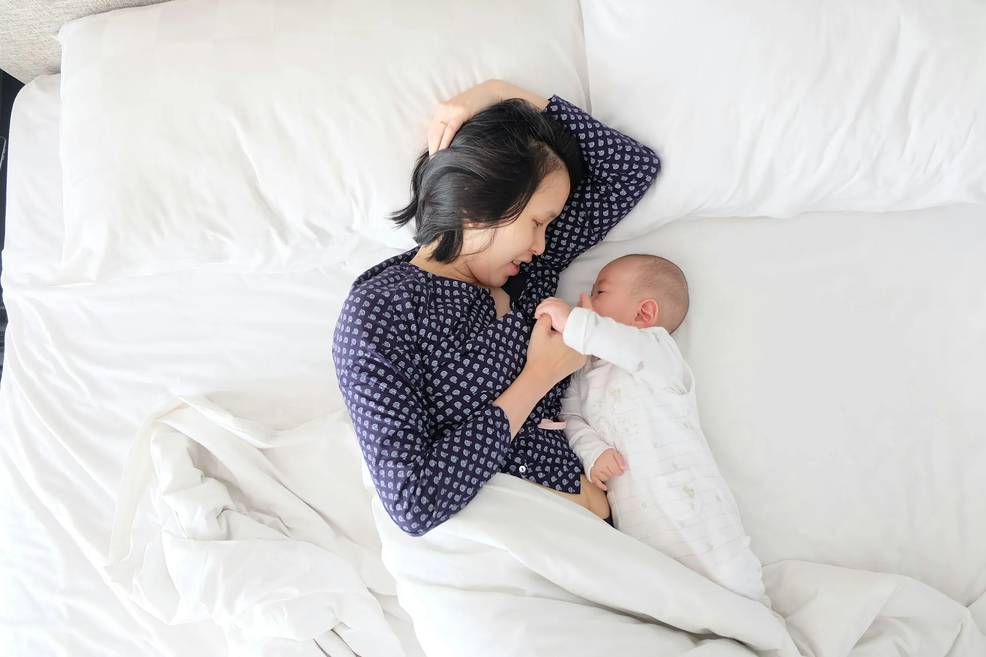 New mother resting in a white bed next to her sleeping newborn