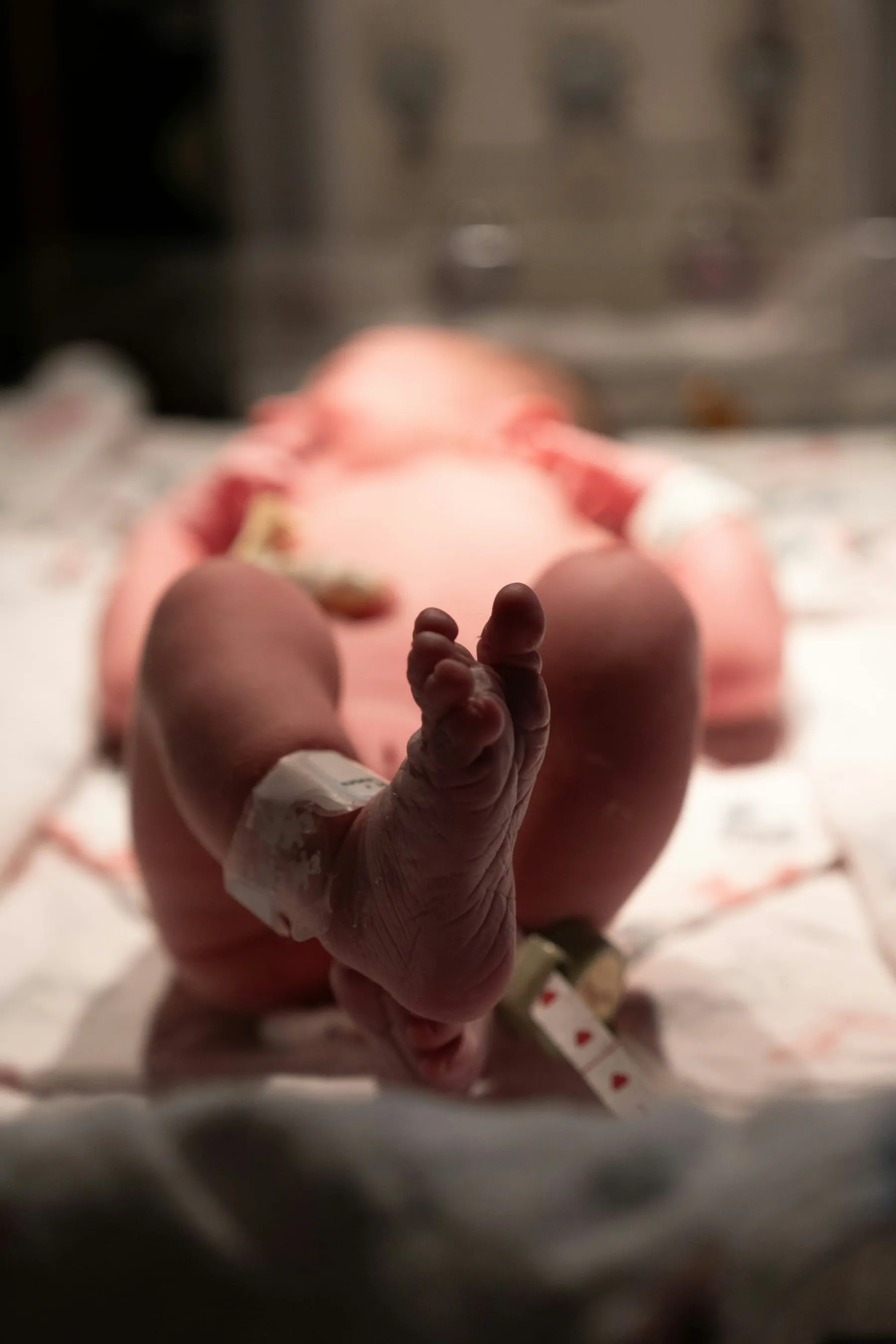 A newborn's tiny foot raised in a hospital bassinet, with a hospital ID band around the ankle