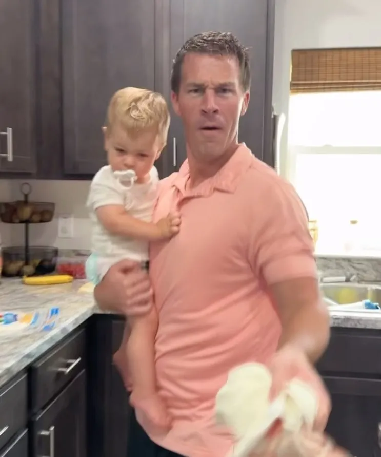 Dad pulling a face in the kitchen with his toddler on one arm